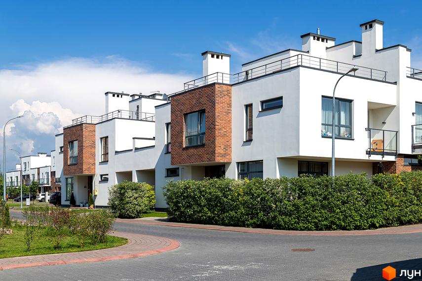 Котеджне містечко Липові Роси. Зовнішній вигляд новобудов з білими фасадами та цегляними вставками, огороджені кущами. Автомобілі та дорога на прибудинковій території.