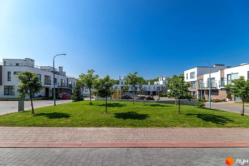 Котеджне містечко КМ Липові Роси. Білі двоповерхові будинки з балконами та цегляними елементами, зелена галявина з деревами та дитячий майданчик.