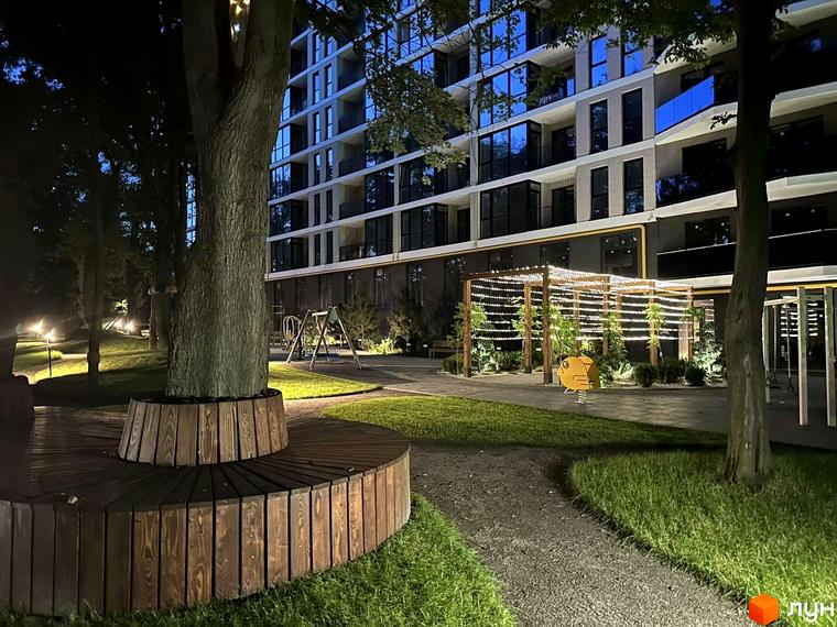 Житловий комплекс Tiffany: багатоповерховий будинок з великими вікнами та балконами, освітлена прибудинкова територія з деревами та дитячим майданчиком.
