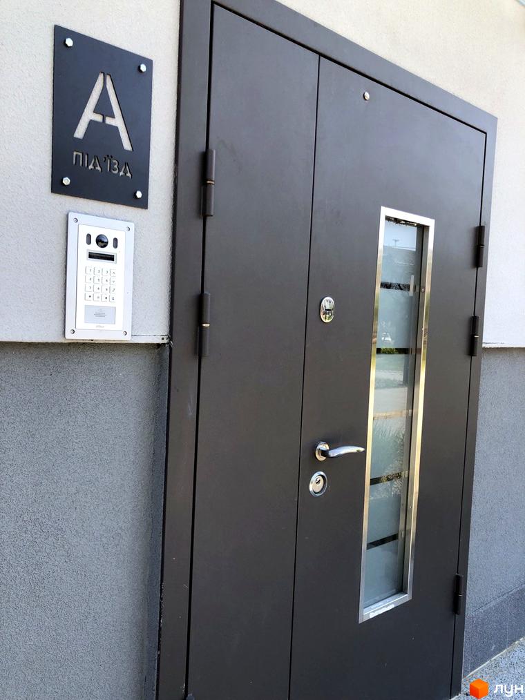 Вхідна група в Новобудові Сучасний: двері з домофоном та інформаційною табличкою з номером під'їзду. Фасад будинку з оздобленням.
