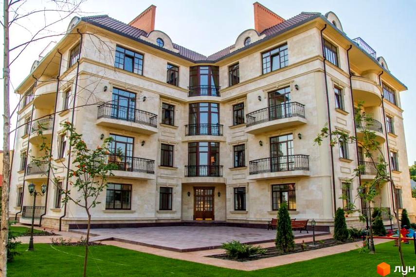 Клубний будинок „Ліон“ з кам'яним фасадом та балконами. Прибудинкова територія з газоном та деревами.