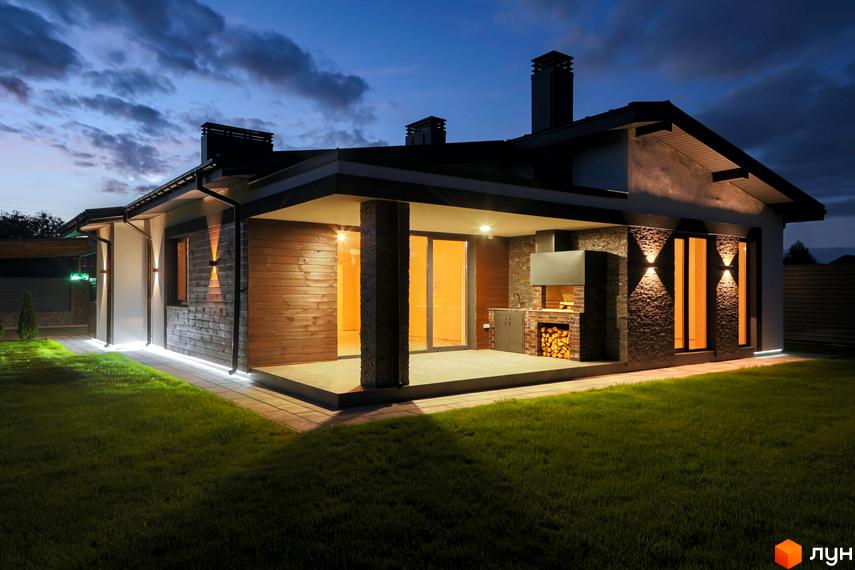 Котеджне містечко КМ New Village: одноповерховий будинок з дерев'яним фасадом та зоною барбекю, освітлена прибудинкова територія з газоном.