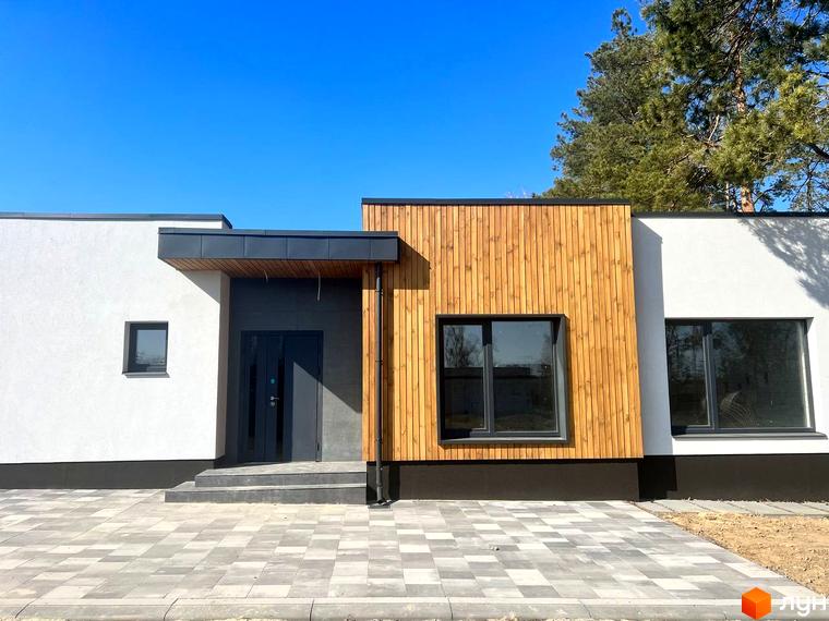 Будинок житлового комплексу VISION з білим фасадом, дерев'яним оздобленням та темними вікнами. Перед будинком вимощена бруківкою територія.