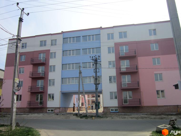 Житловий комплекс Твій дім: фасади будинку в рожевих, білих та блакитних тонах, з балконами та великими вікнами. Навколо будинку видно прибудинкову територію та дорогу.