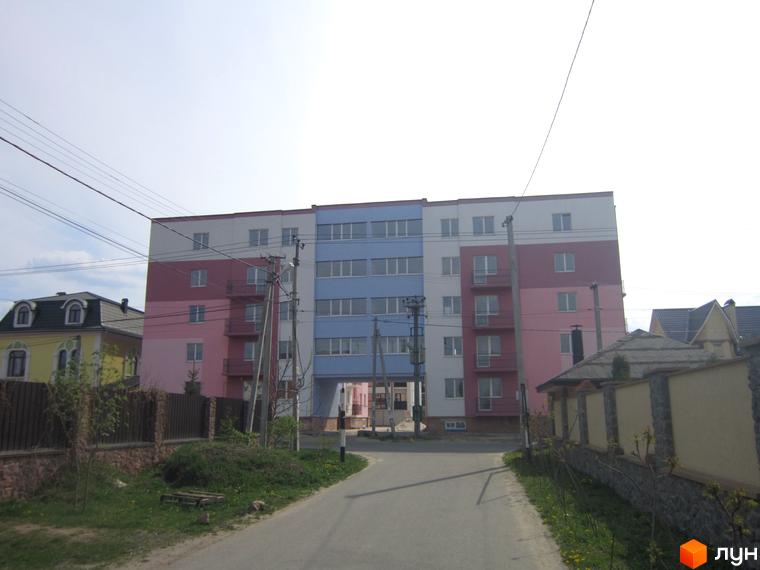 Будівельний проєкт Твій дім: багатоповерховий будинок з рожевими, білими та блакитними фасадами, аркою між секціями та прибудинковою територією.