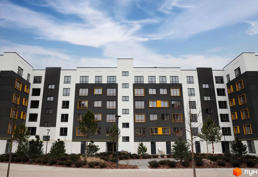 Зовнішній вигляд новобудови ЖК Молодість з сірими та білими фасадами, жовтими вікнами та прибудинковою територією з деревами та кущами.