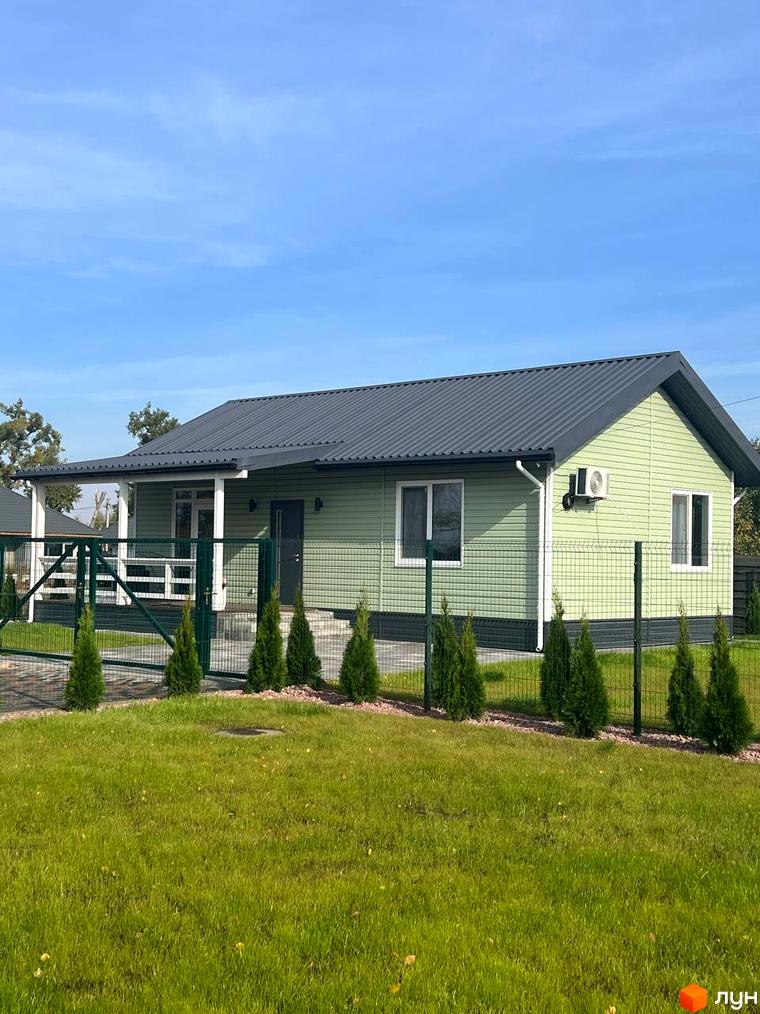 Зовнішній вигляд будинку в Котеджному містечку Lagom Village. Зелений газон перед будинком та декоративні туї вздовж огорожі.