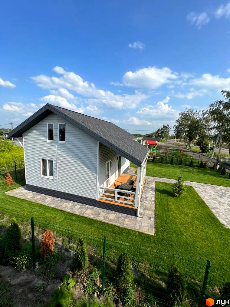 Вигляд котеджу в Котеджному містечку Lagom Village з великою терасою та зеленим газоном. На задньому плані дитячий майданчик.