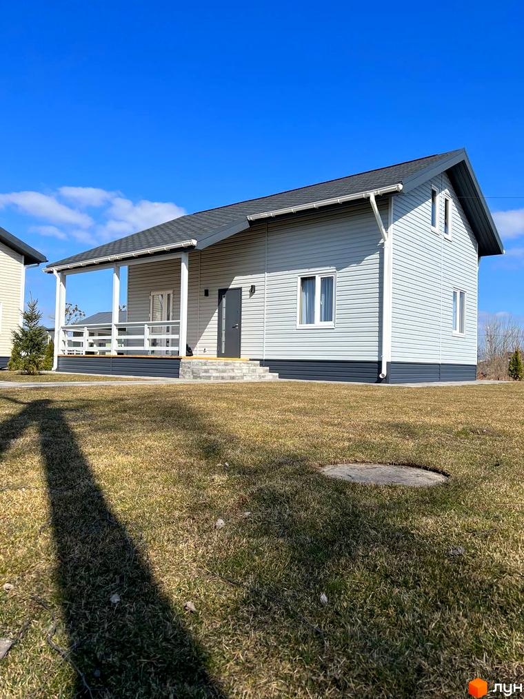 Зображення будинку з сірим фасадом та білою верандою в Котеджному містечку Lagom Village. Зелена галявина перед будинком.