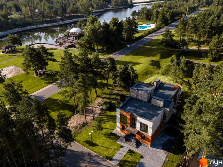 Вигляд з висоти на Котеджне містечко Riviera Village. Двоповерховий будинок з сірою плиткою та великою прибудинковою територією з газоном.