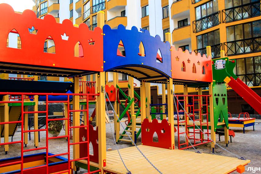 Дитячий майданчик у житловому комплексі Щасливий на Петропавлівці. Яскравий майданчик з гірками, драбинками та пісочницею на тлі багатоповерхових будинків.