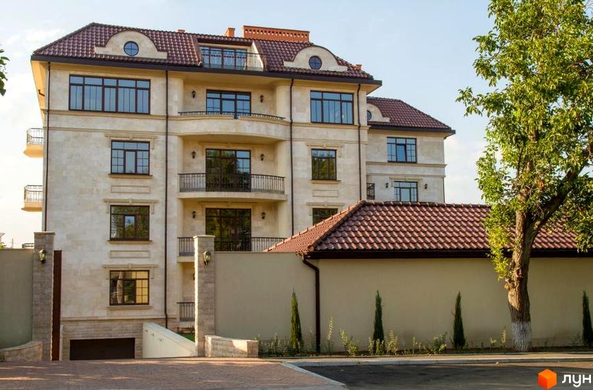 Клубний будинок „Ліон“ з елегантною світлою фасадною обробкою та коричневим черепичним дахом. Навколо будинку розташована охайна прибудинкова територія з деревами та парканом.