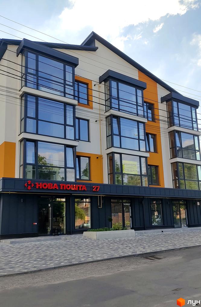 Фасад новобудови на вул. Трамвайна, 36 з великими вікнами та оранжевими елементами. Біля будинку викладена бруківка.