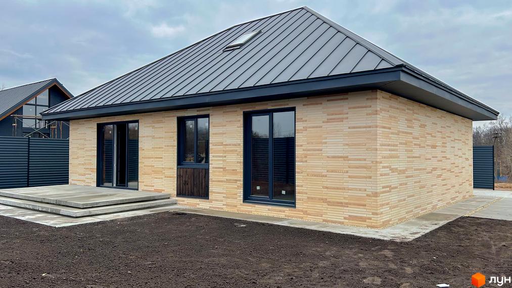 Котеджне містечко КМ SMADE Park: одноповерховий будинок з світлої цегли, сірим дахом та великими вікнами. Поруч облаштований бетонний двір та зелена ділянка.