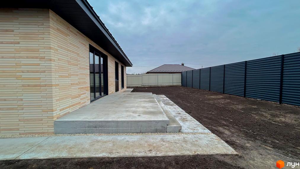 Котеджне містечко SMADE Park: фасад будинку з світлої цегли та прибудинкова територія з бетонованим патіо та парканом.