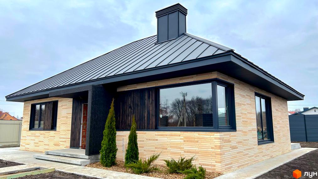 Котеджне містечко SMADE Park: одноповерховий будинок з світлою цегляною облицовкою, темною черепицею та великими вікнами. Навколо будинку зелені насадження та бетонні доріжки.