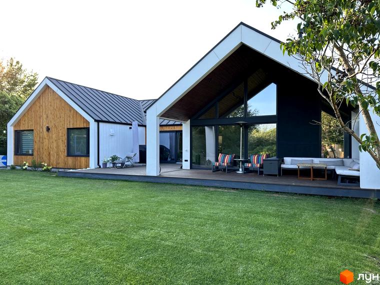 Котеджне містечко КМ Norway Village: двоповерховий будинок з дерев'яним фасадом та великими вікнами, зелена галявина та тераса з вуличними меблями.