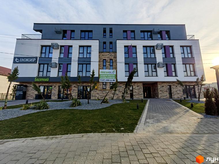 Зовнішній вигляд житлового комплексу ІНЖИР з фасадом білого та сірого кольорів, вікнами з фіолетовими вставками та прибудинковою територією з газоном та доріжками.