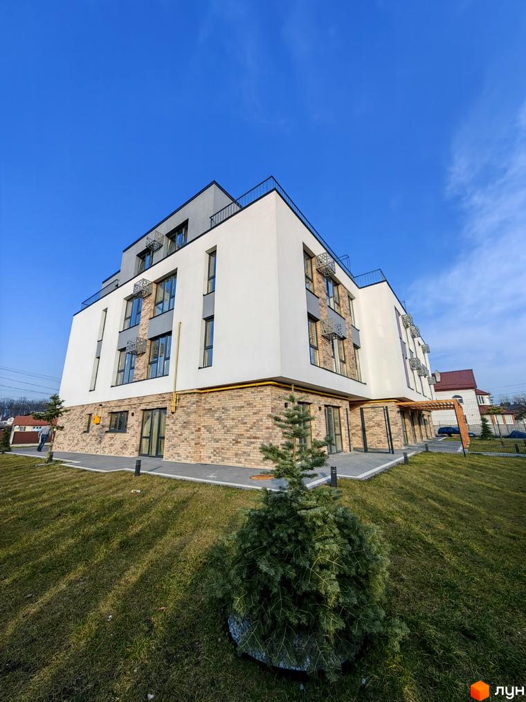 Зображення фасаду будинку Житлового комплексу ІНЖИР з облицюванням з цегли та білими стінами. Навколо будинку зелений газон.