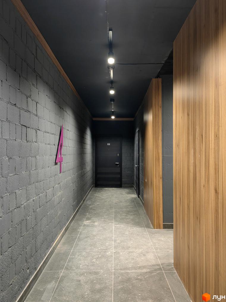 Коридор новобудови ЖК ІНЖИР з сірою цегляною стіною та дерев'яними панелями. Стильний дизайн інтер'єру.