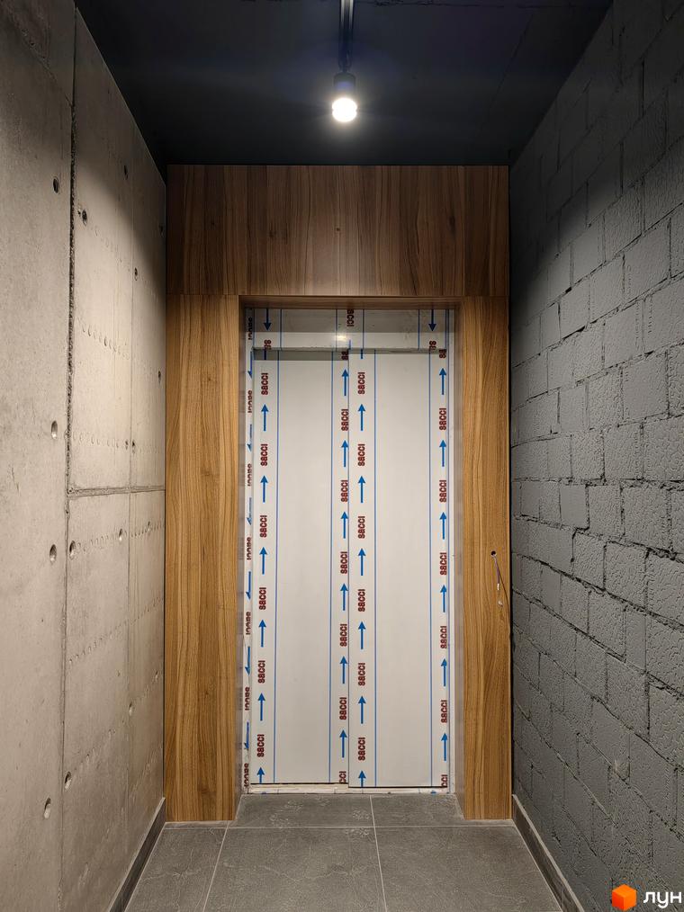 Вхідна група житлового комплексу ІНЖИР з оздобленням під дерево та бетонними стінами.