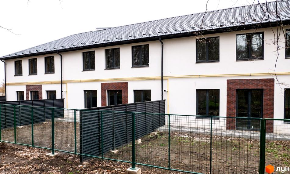 Зовнішній вигляд будинку в Містечко котеджів ПРОСТІР з білими стінами, темними вікнами та дахом. Перед будинком розташовано зелений паркан та доглянута прибудинкова територія.