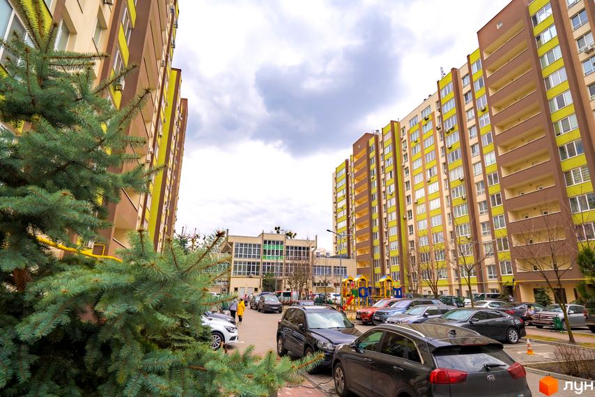 Житловий комплекс Софіївський квартал на вулиці Ак. Шалімова. Багатоповерхові будинки з коричнево-зеленими фасадами та балконами, дитячий майданчик та парковка з автомобілями.