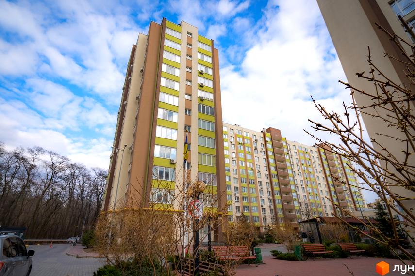 Зовнішній вигляд багатоповерхового будинку ЖК Софіївський квартал на вул. Ак. Шалімова з зеленими та бежевими фасадами. На прибудинковій території видно дерева та лавки.