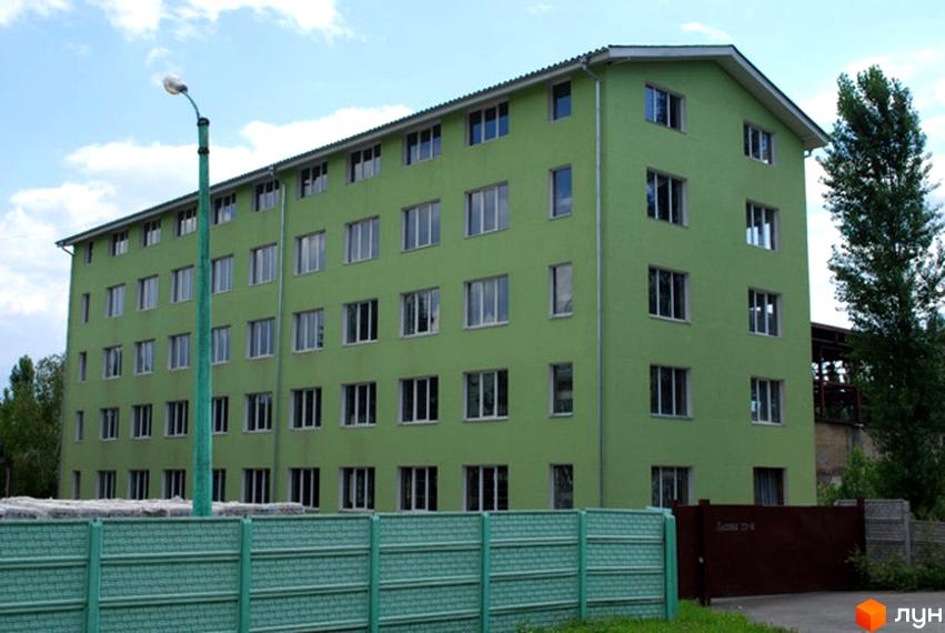 Зовнішній вигляд ЖК Жовтень – цегляна будівля з зеленим фасадом та численними вікнами. Перед будинком розташована зелена огорожа та вуличне освітлення.