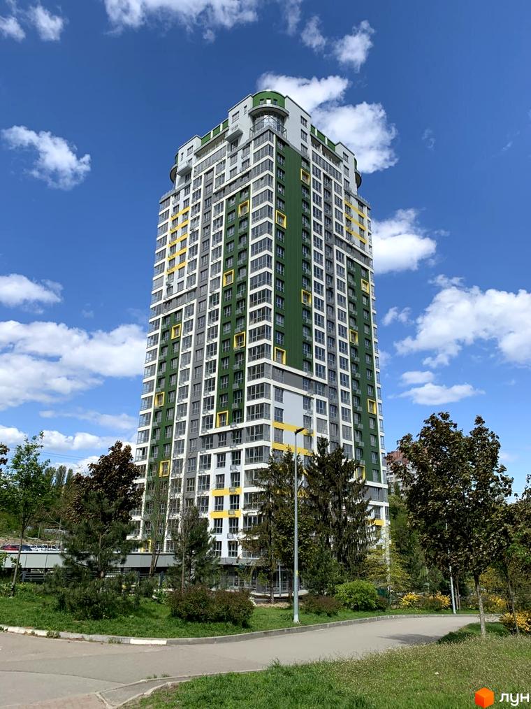 Житловий комплекс Паркове місто: висотна будівля з фасадом зеленого, білого та жовтого кольорів. Навколо зелена територія з деревами та доріжками.