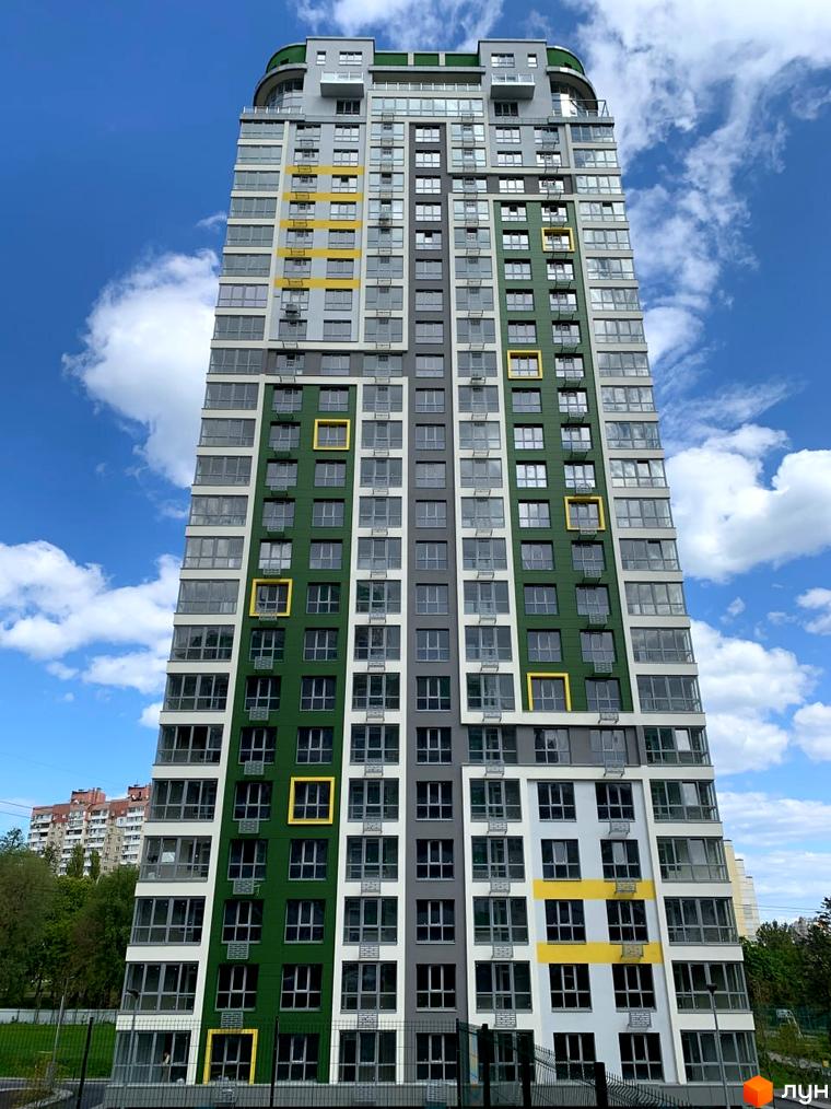 Багатоповерховий будинок Житлового комплексу Паркове місто з зеленим, сірим та білим фасадом, жовтими акцентами. Навколо зелені насадження та блакитне небо.