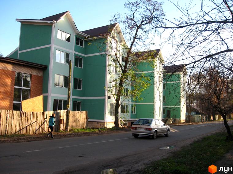 Зовнішній вигляд новобудови ЖК Green House з зеленими фасадами та білими декоративними елементами. Поруч дорога з автомобілем та пішохід.