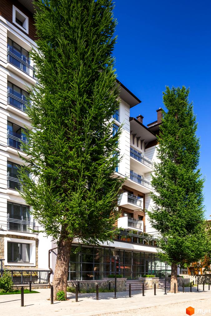 Зовнішній вигляд новобудови ЖК Крайобраз з фасадом білого кольору та балконами. Навколо будівлі ростуть зелені дерева, створюючи приємний ландшафт.