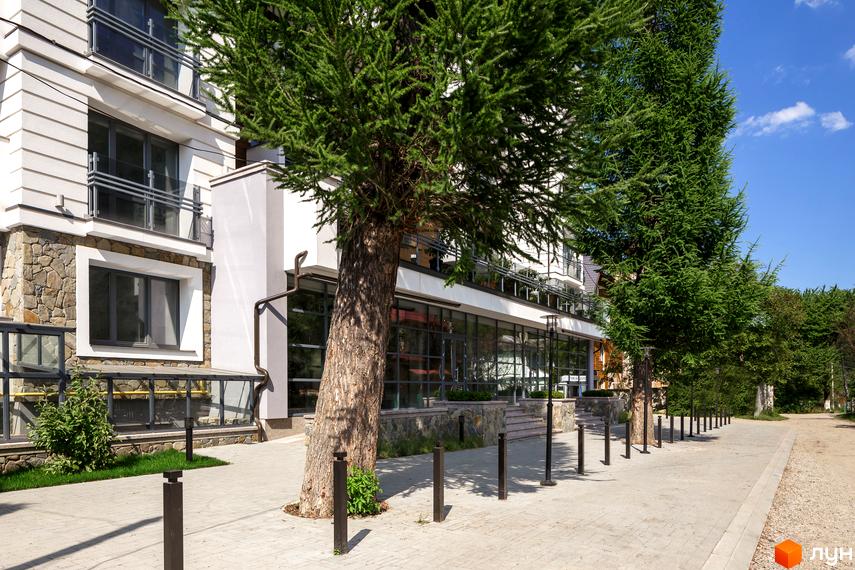 Житловий комплекс Крайобраз: фасади будівель з кам'яним оздобленням та скляними елементами. Прибудинкова територія з деревами та бруківкою.