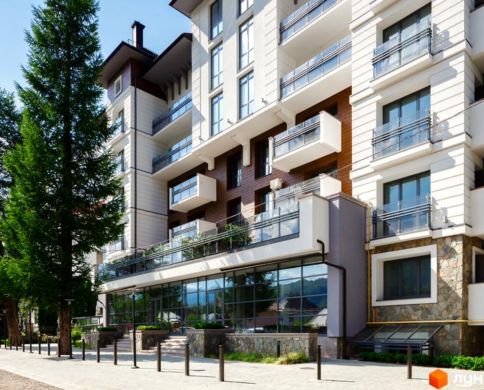 Зовнішній вигляд новобудови ЖК Крайобраз з великою кількістю скляних балконів та панорамних вікон. Навколо будівлі облаштований тротуар та зелені насадження.