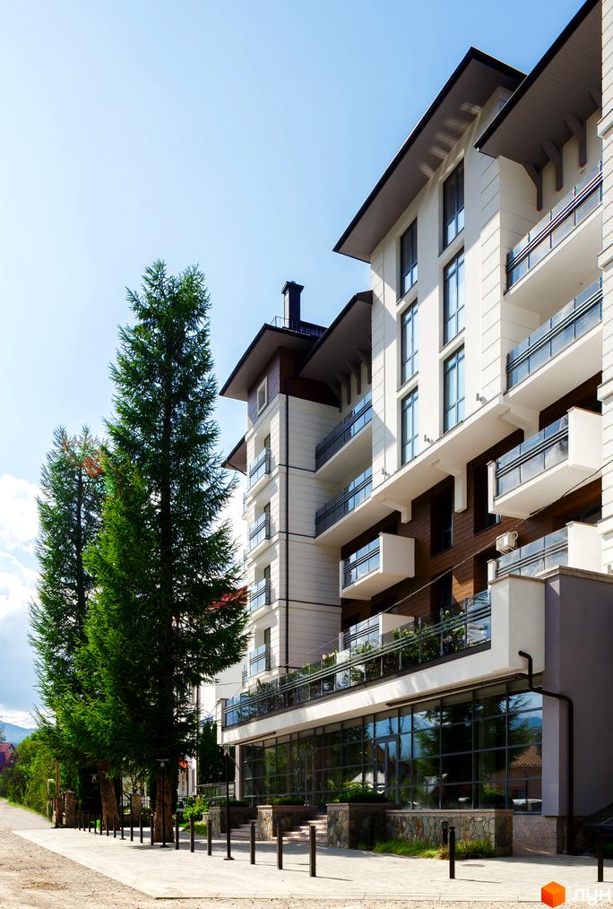 Зовнішній вигляд новобудови ЖК Крайобраз з елементами дерева та скляними балконами. Поруч розташована доглянута прибудинкова територія з деревами та тротуаром.