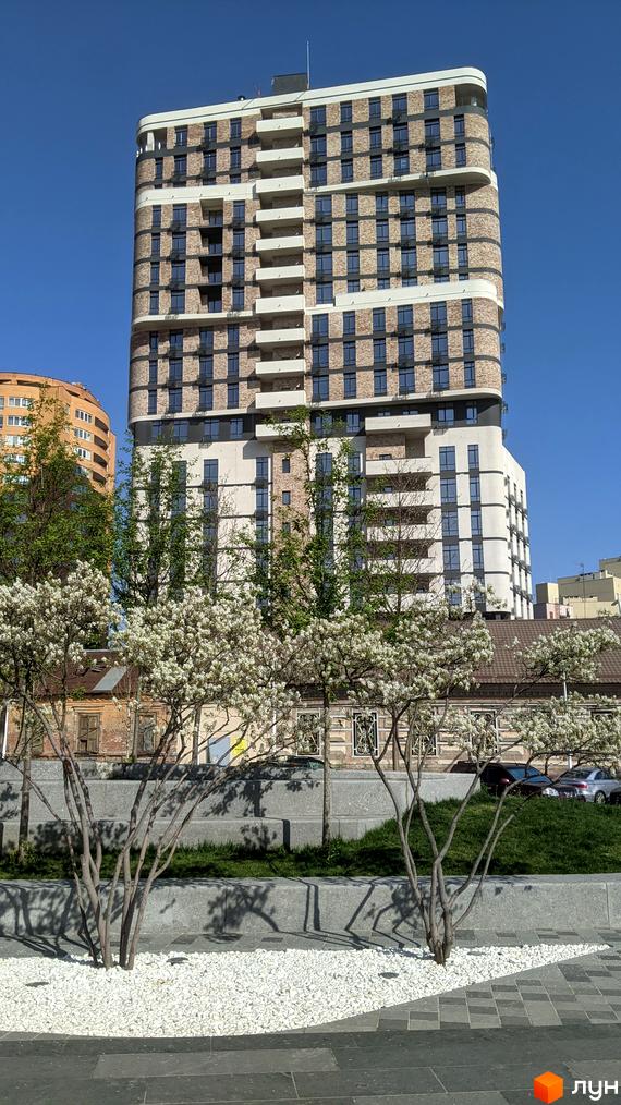 Житловий комплекс Loft White: висотна будівля із заокругленими кутами, цегляною текстурою та світлими елементами. Навколо – квітучі дерева та ландшафтний дизайн з білим камінням.
