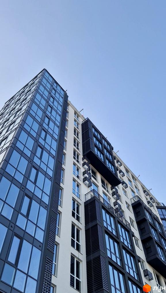 Новобудова Янтарний: багатоповерховий будинок з комбінованим фасадом, великими блакитними вікнами та виступаючими темними елементами.