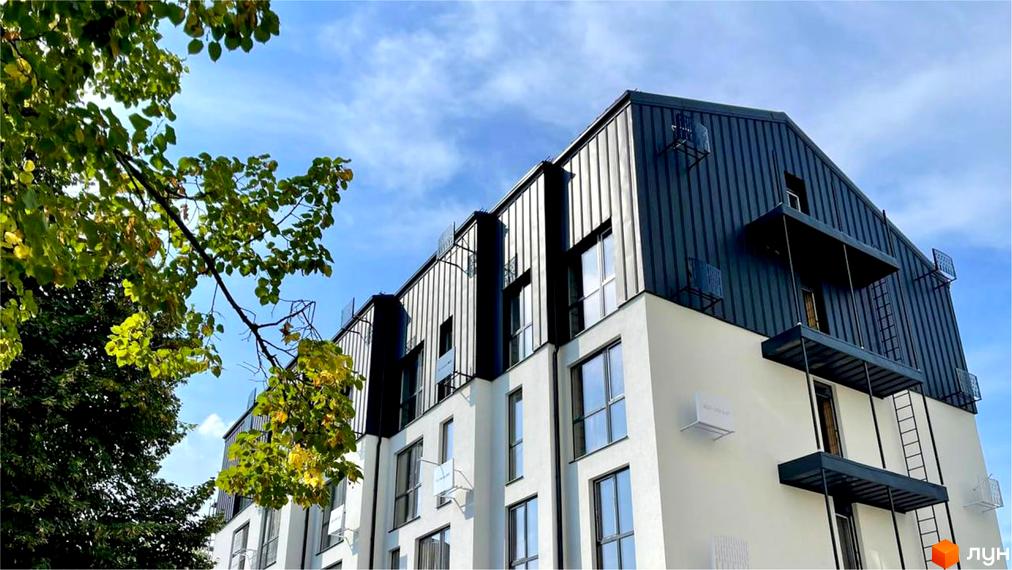 Будівля житлового комплексу Coliving EST з білими нижніми поверхами та темним металевим облицюванням верхньої частини, поруч зелені дерева.