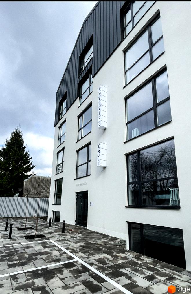 Зображення новобудови Coliving EST з білим фасадом, темною обшивкою та великими вікнами. На прибудинковій території видно бруківку та розмітку.