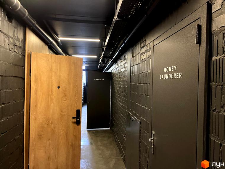 Внутрішній коридор з темними цегляними стінами та різними дверима у житловому комплексі Coliving EST.