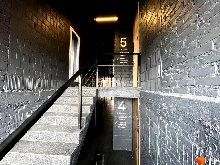 Сходи в житловому комплексі Coliving EST з сірими цегляними стінами та вказівниками поверхів. Сучасний дизайн інтер'єру коридору.