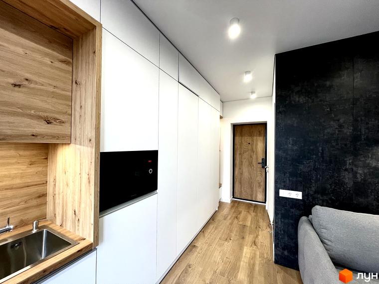 Інтер'єр квартири в Coliving EST з вбудованою кухнею, білими шафами та світлим дерев'яним покриттям підлоги.
