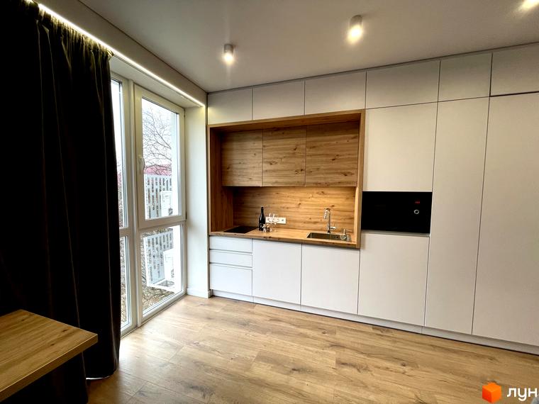 Інтер'єр кухні в житловому просторі Coliving EST з білими шафами, дерев'яною робочою зоною та великим вікном.