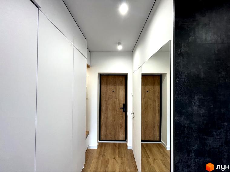 Коридор у Coliving EST: світлий простір з білими шафами, дерев'яною підлогою та великим дзеркалом.