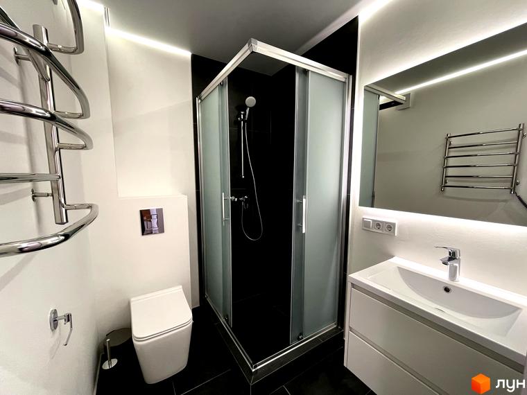 Інтер'єр ванної кімнати в Coliving EST: душова кабіна, білий унітаз, умивальник з дзеркалом та підсвічуванням.