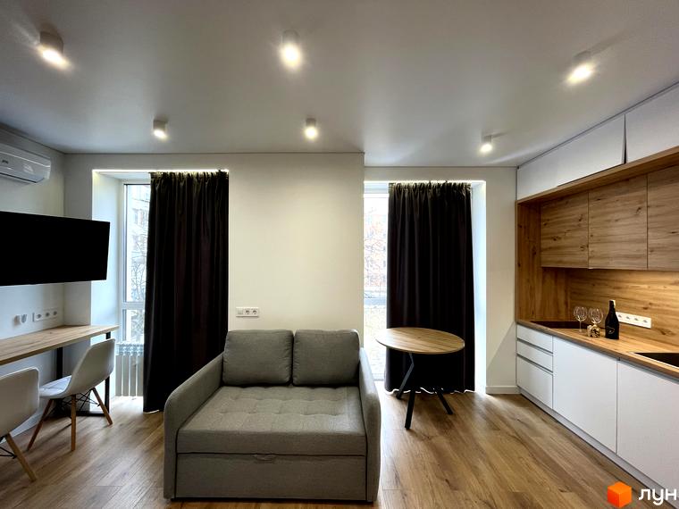 Сучасний інтер'єр квартири в Coliving EST з диваном, робочим столом та кухнею. Простора вітальня з великими вікнами та темними шторами.