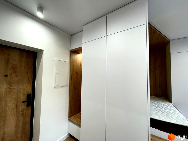 Вхідна зона житлового комплексу Coliving EST з дерев'яними дверима, білими вбудованими шафами та функціональною нішею.