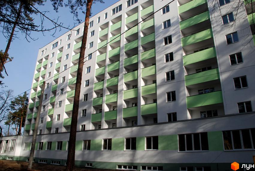 Житловий комплекс Сосновий двір. Багатоповерховий будинок з зеленими балконами та білими фасадами, розташований серед дерев.