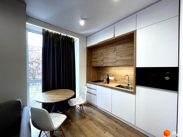 Кухня-вітальня в апартаментах Coliving EST з білими меблями, дерев'яними елементами та обідньою зоною біля вікна.